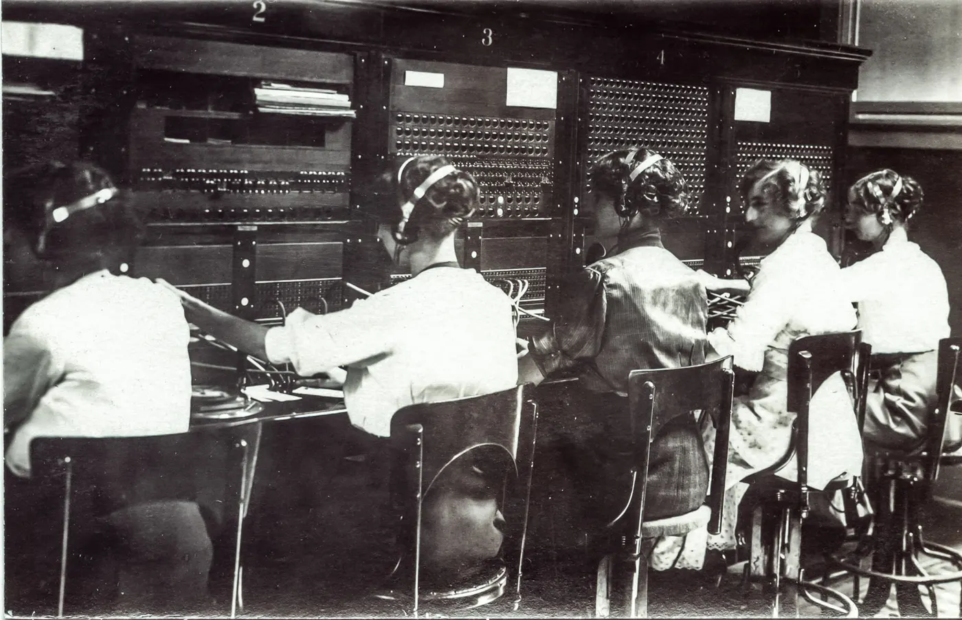 Five telephone operators at a switchboard, plugging calls through by hand